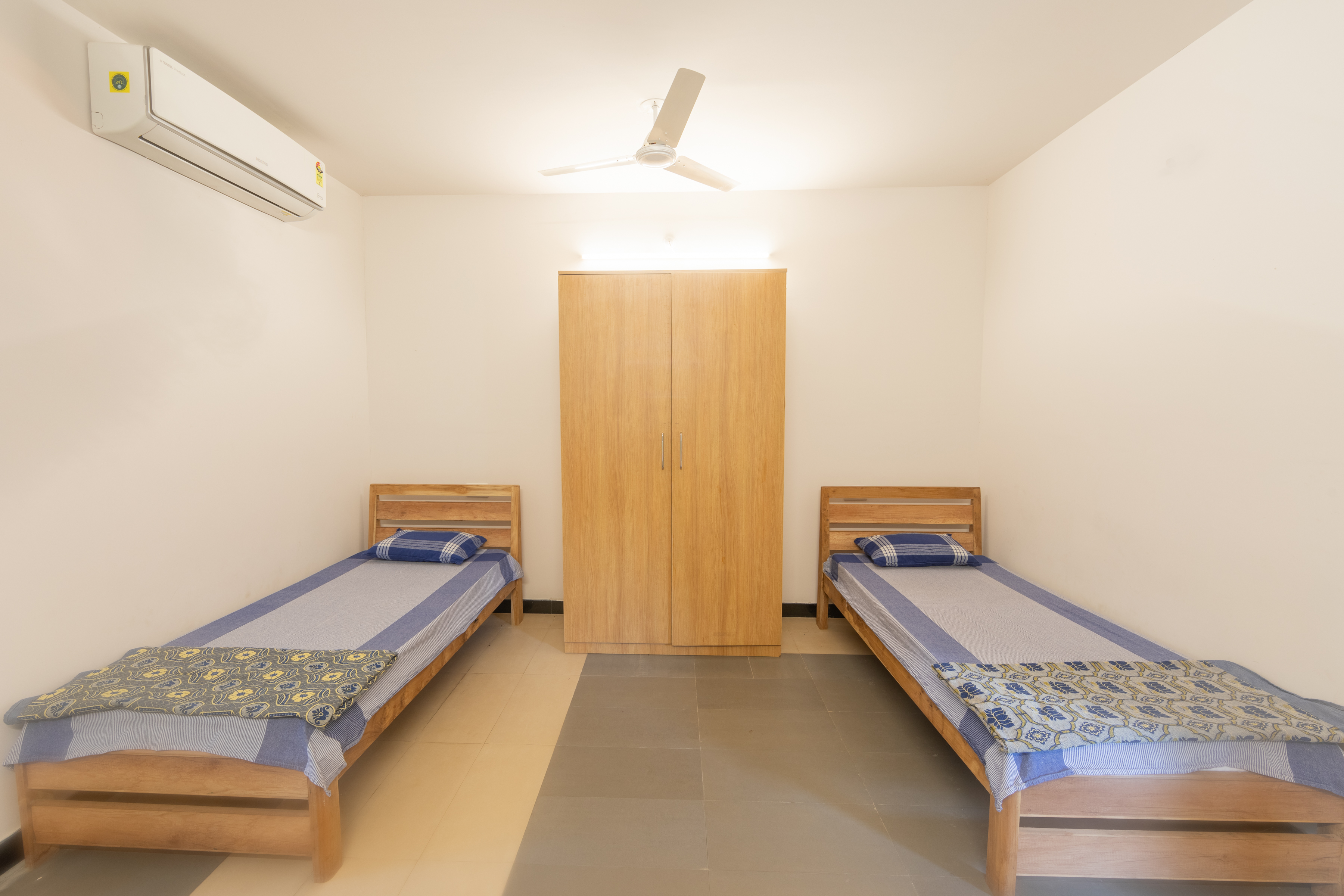 A guest room at Freshwater: two beds, a full-height wardrobe, a desk with a kettle and a window onto the trees.